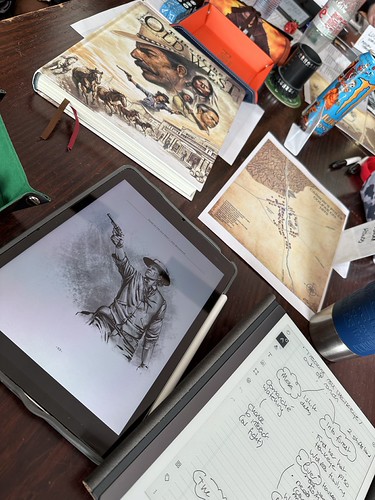 The Tales of the Old West roleplaying game at the table during Furnace. An iPad is open on the image of a gunslinger in the QuickDraw PDF, and alongside it is a reMarkable 2 with scenario notes. At the top of the table is the rule book and a map titled Carson's Folly, Colfax County, 1873.